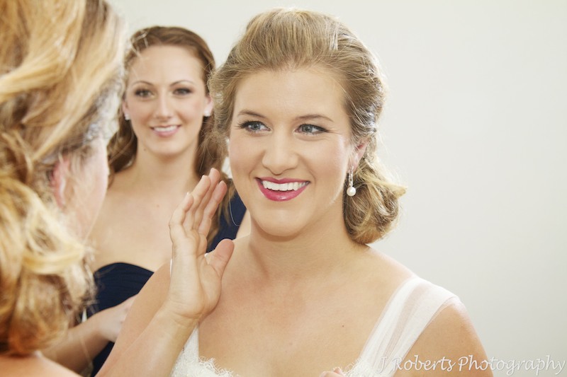 Bride putting earrings on in mirror with bridesmaid watching - wedding photography sydney